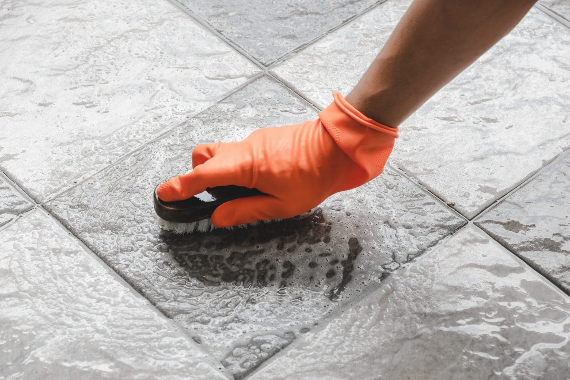 Gloved hand scrubbing grout between floor tiles